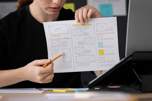 Designer pointing a pencil at a paper wireframe layout during a design review