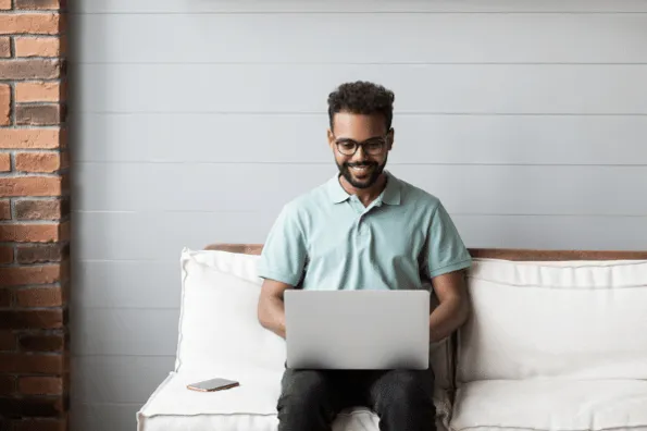 Man smiling while using a laptop on a couch